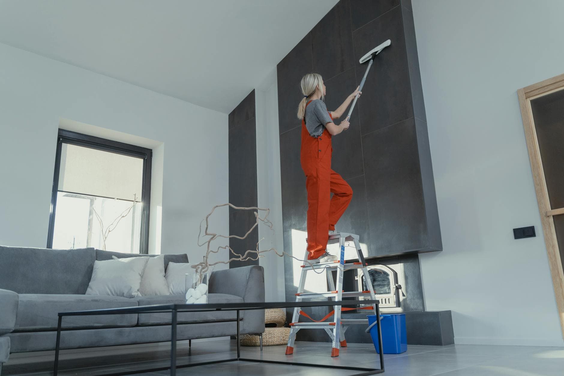 NYC Maid cleaner in red overalls on a ladder cleaning a high wall in a Manhattan apartment — Office Cleaning in Red Hook, Brooklyn
