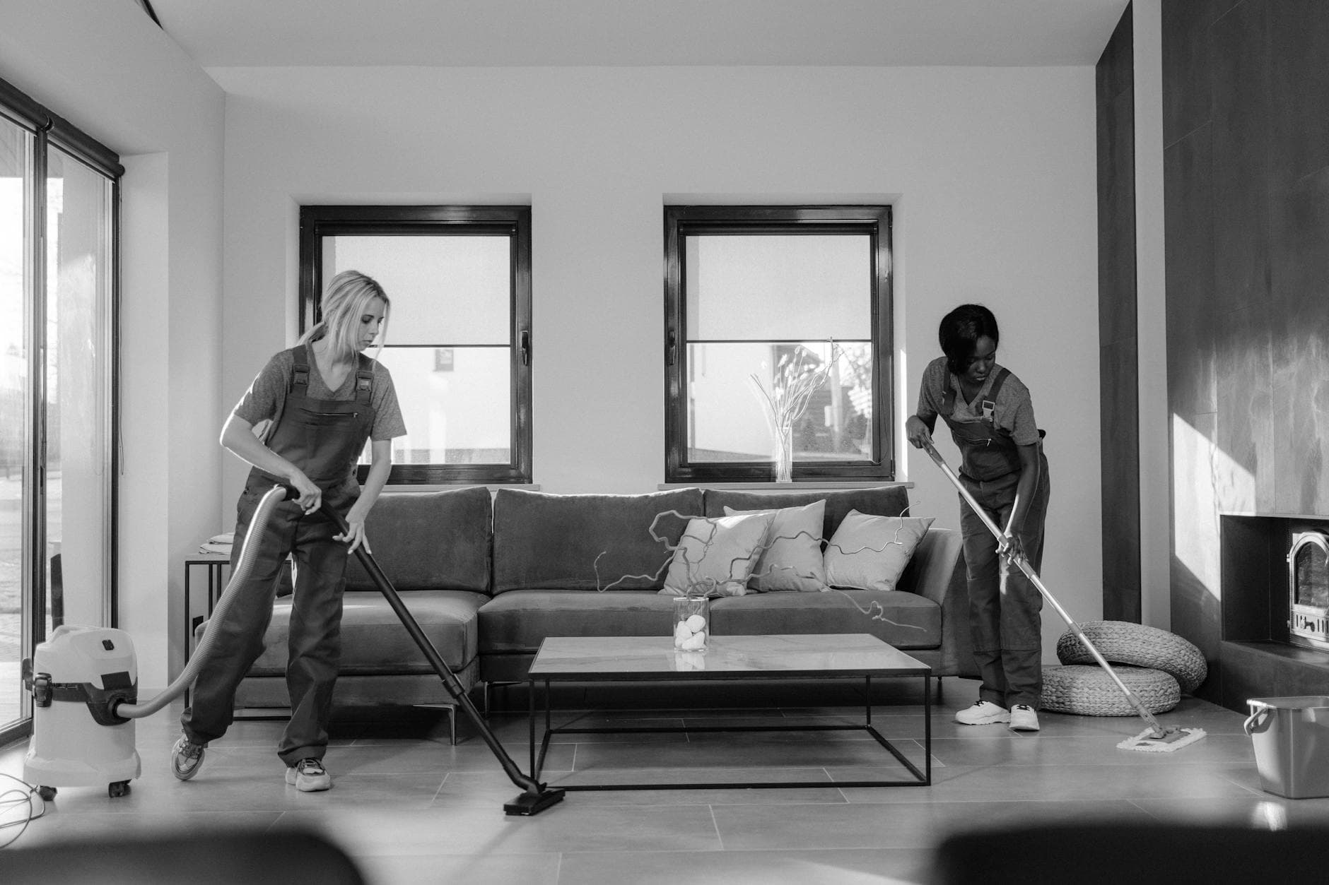Two NYC Maid cleaners in work uniforms using a vacuum and mop in a modern Manhattan living room — Office Cleaning in Sands Point, Long Island