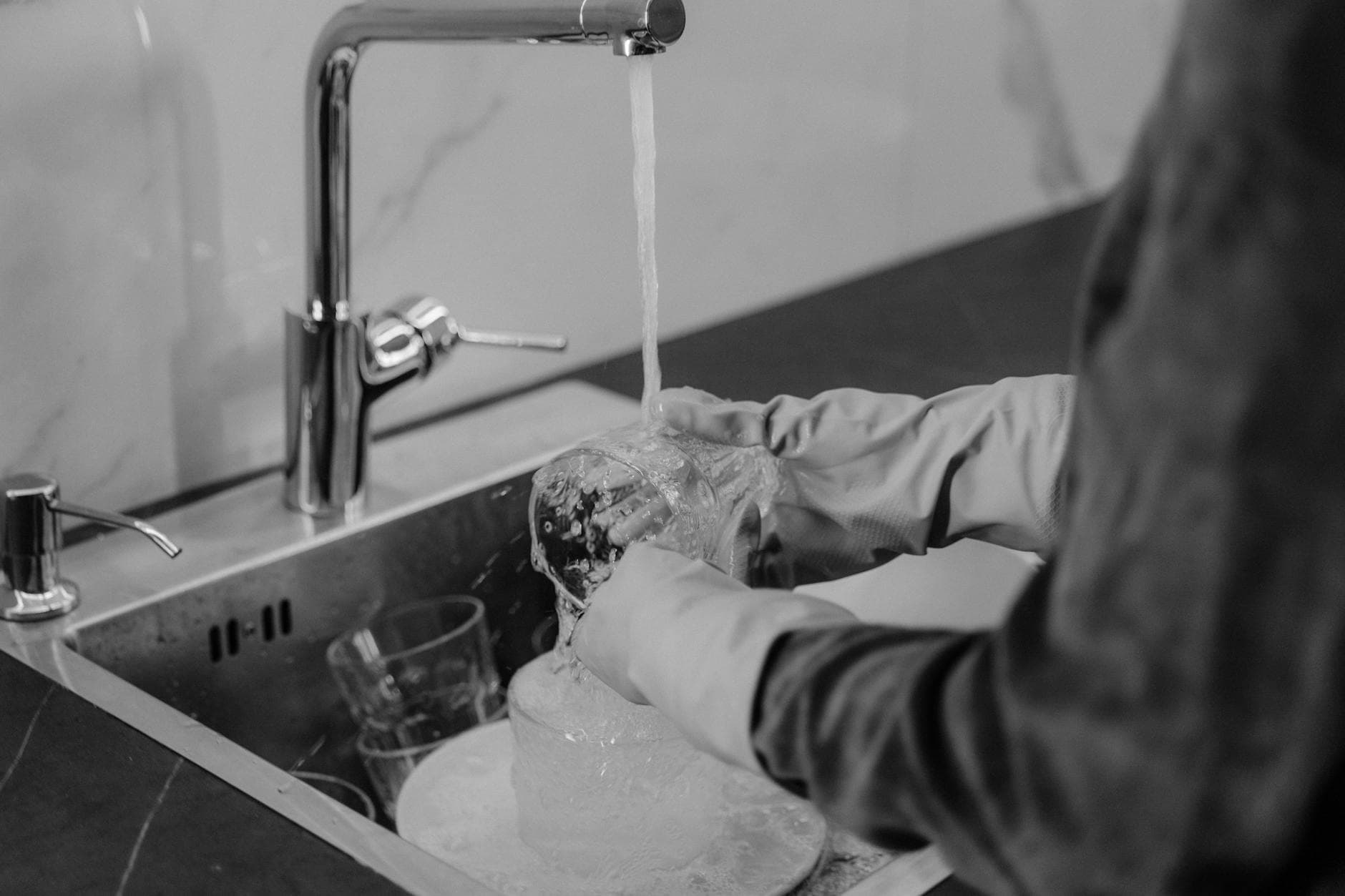 NYC kitchen cleaning service washing dishes under running water at the sink — cleaning services in Manhattan