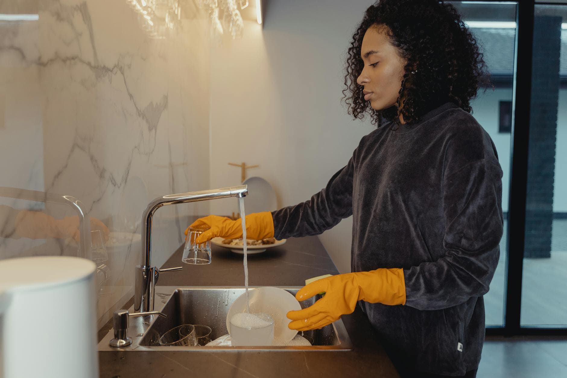 NYC maid wearing rubber gloves washing dishes in a modern Manhattan kitchen — cleaning services in SoHo, Manhattan