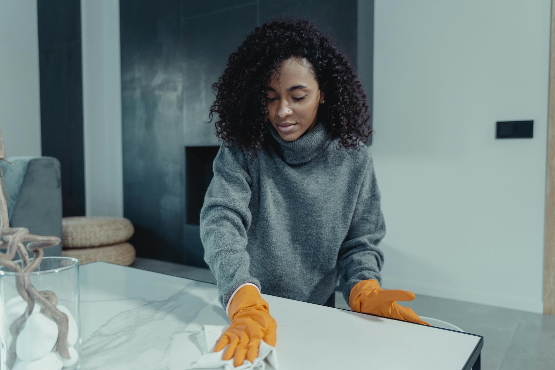 A NYC maid wearing gloves wiping a coffee table in a modern Manhattan living room — cleaning services in Brooklyn